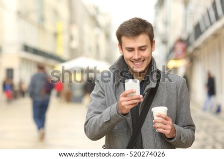 Front view portrait of a businessman walking towards camera and using a smart phone in the street in winter