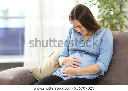 Pregnant woman suffering belly ache sitting on a couch in the living room at home