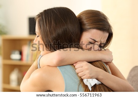 Girl embracing to comfort to her sad best friend after break up sitting on a couch in the living room at home