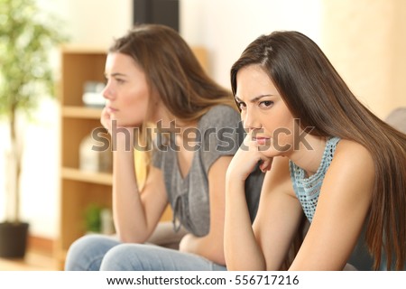 Angry friends or roommates sitting on a sofa in the living room at home