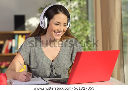 Beautiful portrait of a student learning on line watching video tutorials with a red laptop and headphones in a table at home
