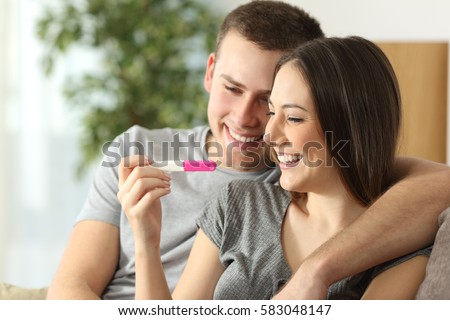 Happy couple checking pregnancy test sitting on a couch in the living room at home