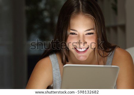 Close up of a single girl watching media content on line in a tablet with the light of the screen in her face in the living room at home