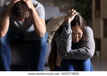 Sad couple after argument or breakup sitting on a sofa in the living room in a house indoor with a dark background
