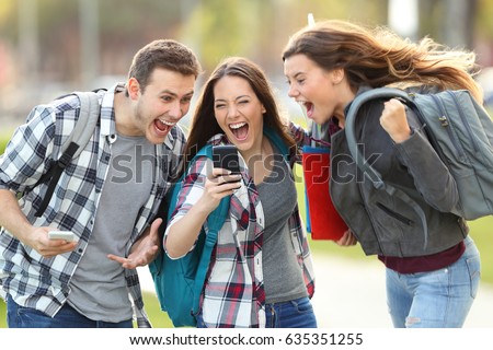 Front view of three excited students receiving good news on line in a mobile phone in an university campus or street