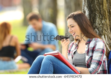 Student using voice recognition with a smart phone to record notes sitting on the grass in a park