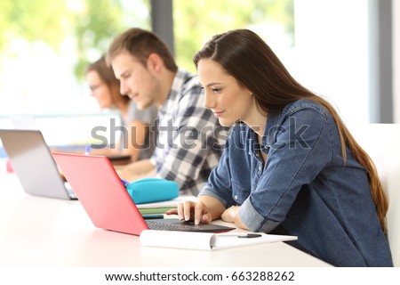 Side view of three attentive students e-learning on line with laptops sitting in a classroom