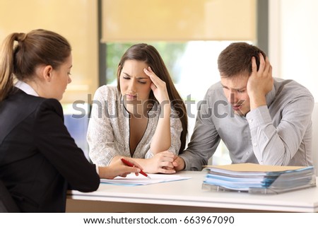 Saleswoman explaining conditions of a document with bad news to a couple of worried customers at office