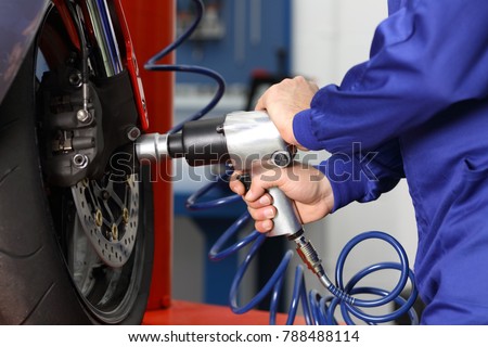 Close up of a motorcycle mechanic hands using a pneumatic gun to loosen a wheel nut in a mechanical workshop