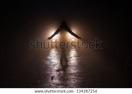 In the forest at night. A person stands on the road in front of the car