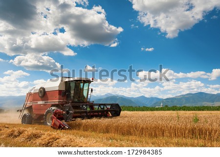 A red harvester in work with mountains in background