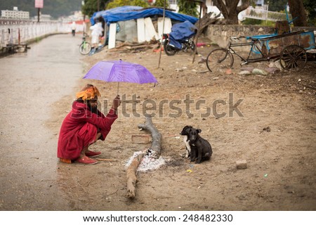 RISHIKESH, INDIA - JAN 02: An unidentified sadhu baba get warming on fire with two small dogs on January 02, 2015. Rishikesh it\'s a spiritual city where you can find many sadhu baba.