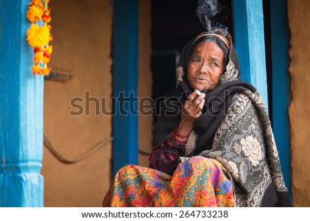HIMALAYAN VILLAGE, NEPAL - NOVEMBER 25: Unkown woman sitting and smoking in fron of traditional house of Himalayan Village on November 25, 2014 in HIMALAYAN VILLAGE, Nepal