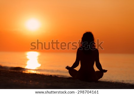 Silhouette of woman in yoga lotus meditation position front to seaside on sunrise