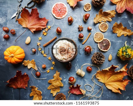 Cozy autumn morning with cup of cocoa with cream and chocolate, dried oranges, cinnamon, nuts and autumn leaves on dark stone background