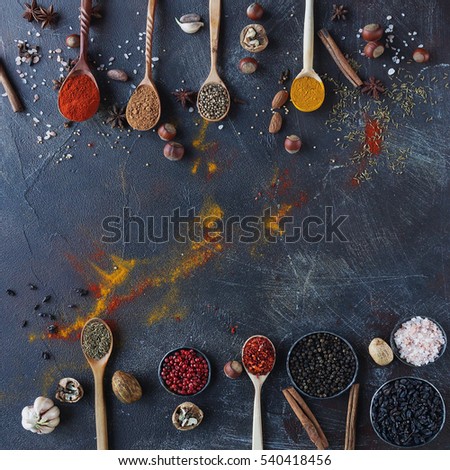 Various indian spices in wooden spoons and metal bowls and nuts on dark stone table. Colorful spices, top view,space for text. Healthy food background.