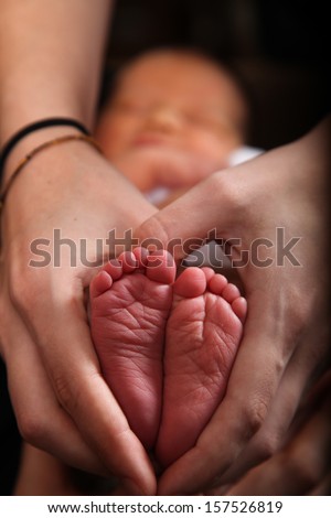 Cute little baby\'s feet are inside a heart made by a mom\'s hands.