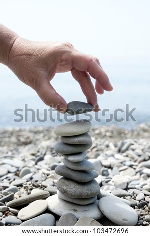 A woman\'s hand put a stone on top of the pyramid of sea stones