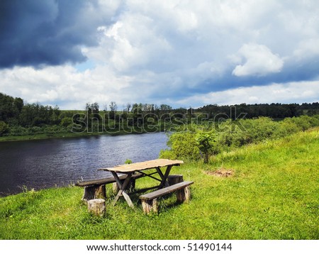 Wooden table and benches on the bank of the summer river
