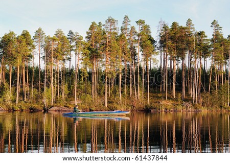 The fisherman floats on a canoe along coast of evening lake