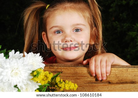 little girl with flowers looking through wooden fence