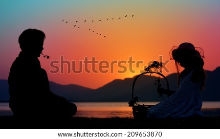 little boy and girl with flowers silhouette; relaxing next to lake