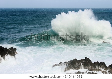 A big wave hitting a rock and crashing into the air