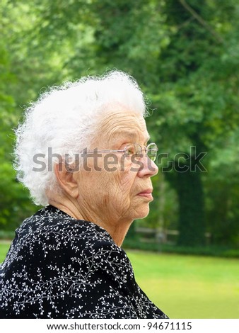 White-haired woman in profile with green trees in background