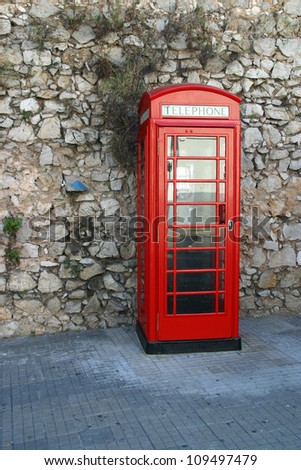 Red telephone box on the street in front of stone wall