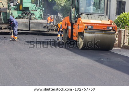 Workers, roller and operating asphalt paver machine during road construction and repairing works