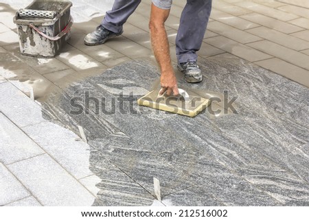 Worker grouting tiles with rubber trowel and gray cement mortar