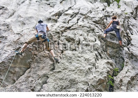 Woman and man rock climbing on a high rock wall