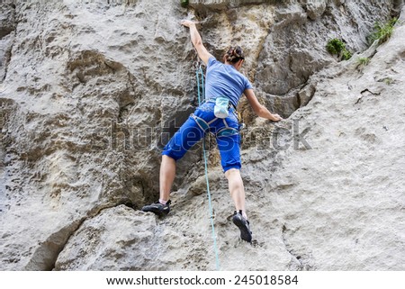 Athletic woman free climbing on a high rock wall