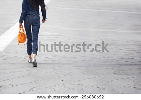 Young slim casual woman with orange leather bag, back view