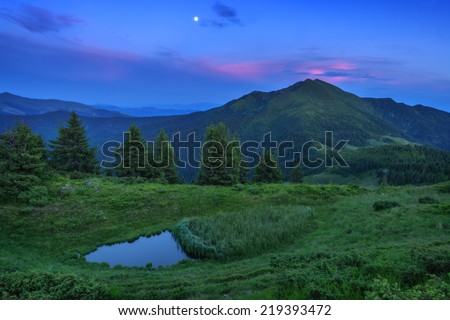 Colorful summer sunset in the Carpathian mountains with small lake and green grass. Marmarosu ridge, Ukraine, Europe.