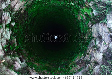 Terrible old deep well with moss. Luminous circle on the bottom