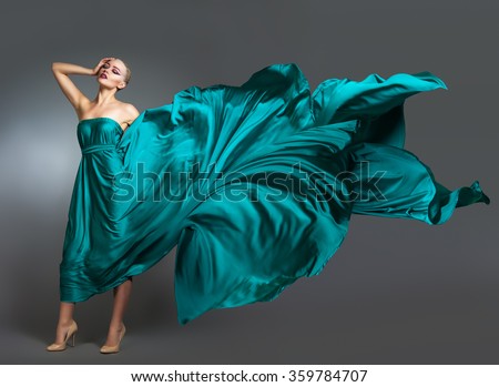 Woman in  silk dress waving on wind. Flying and fluttering gown cloth over gray background Woman Dancing In Fashion Dress