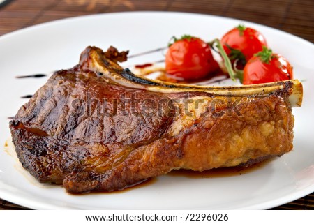 Grilled meat ribs on white plate with tomatoes chives and dark hot sauce
