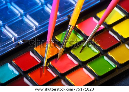Closeup of a palette of watercolor paints with three brushes
