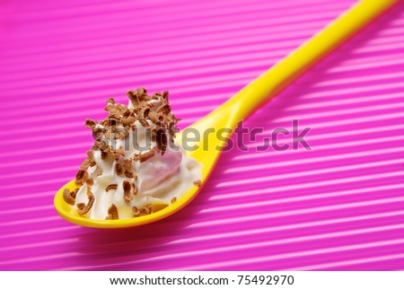 Yellow spoon full of whipped cream with chocolate shavings over pink background. Shallow DOF