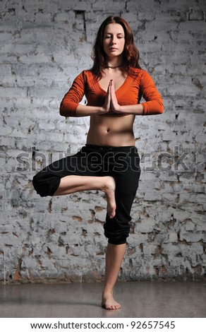 Full-length portrait of young beautiful woman doing yoga excercise against a brick wall