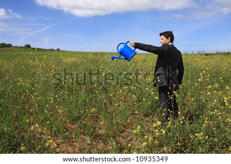 Young business man with a blue watering can in a field