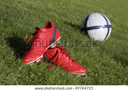Red football shoes and a ball on the grass