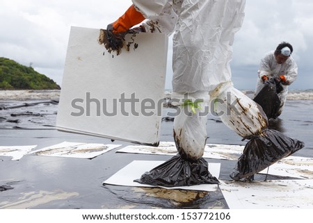 Rayong, Thailand - July 31, 2013: Worker in Biohazard suit placing absorbent paper in a clean-up operation of crude oil spilled at Ao Prao Beach on July 31, 2013 in Koh Samet, Rayong, Thailand.