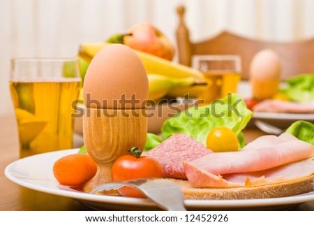 Table served with snacks. Fruits, vegetables, bread, egg, ham etc. Focus on the front egg, shallow depth of field.