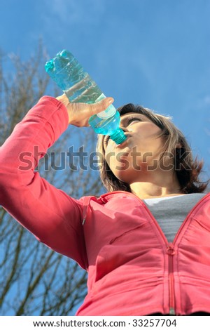 Sportswoman drinking water in a park. View from below.
