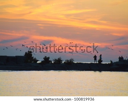 Enchanting sunset over Lake Erie with people walking on rock pier and birds flying