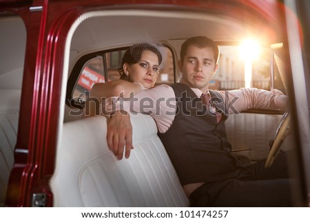 Pretty couple in the vintage car on the sunset background.