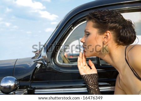 Pretty girl is fixing her make-up near the vintage car.