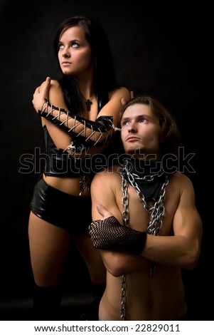 Pretty woman in leather clothing is standing near her slave.